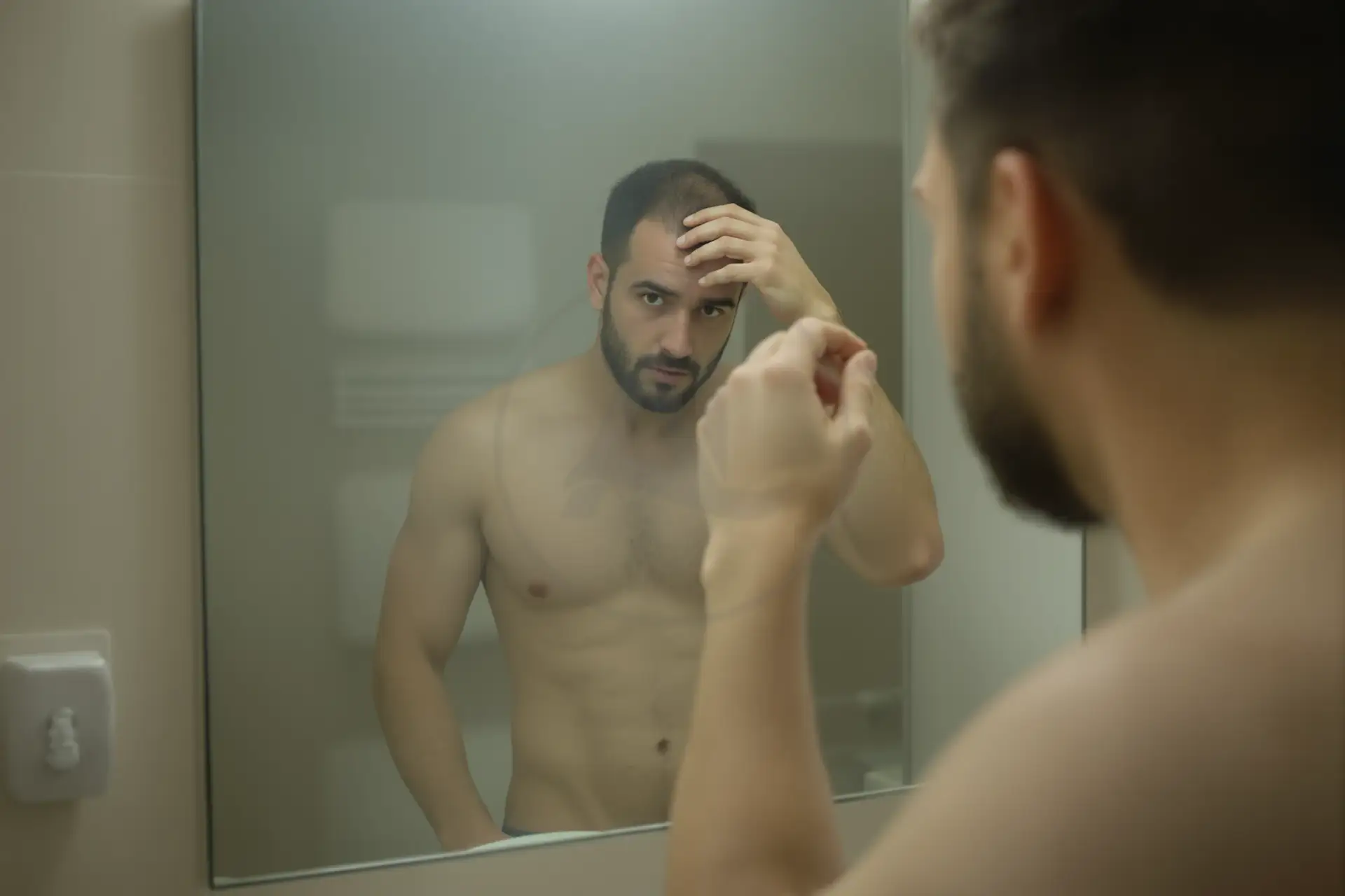 Uomo con diradamento dei capelli si guarda allo specchio in bagno, preoccupato.