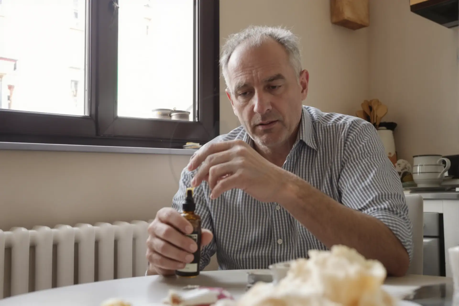 Uomo di mezza età con stempiatura esamina un olio per capelli a casa, luce naturale.