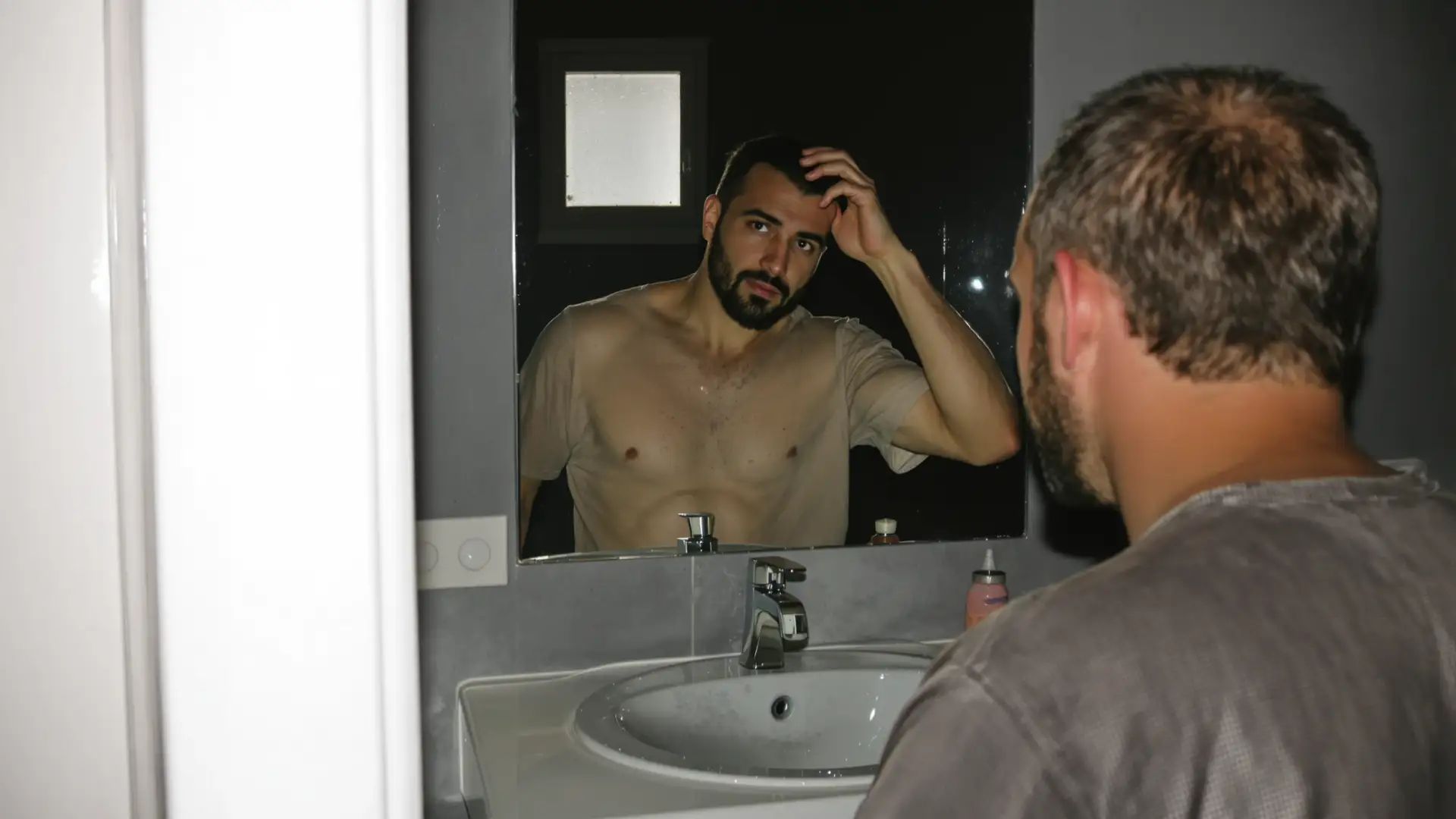 Uomo davanti allo specchio del bagno che si controlla l'attaccatura dei capelli con la mano.