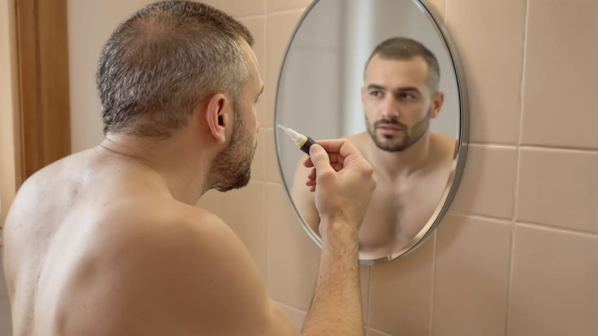 Uomo davanti allo specchio del bagno che applica una fiala anticaduta sul cuoio capelluto.