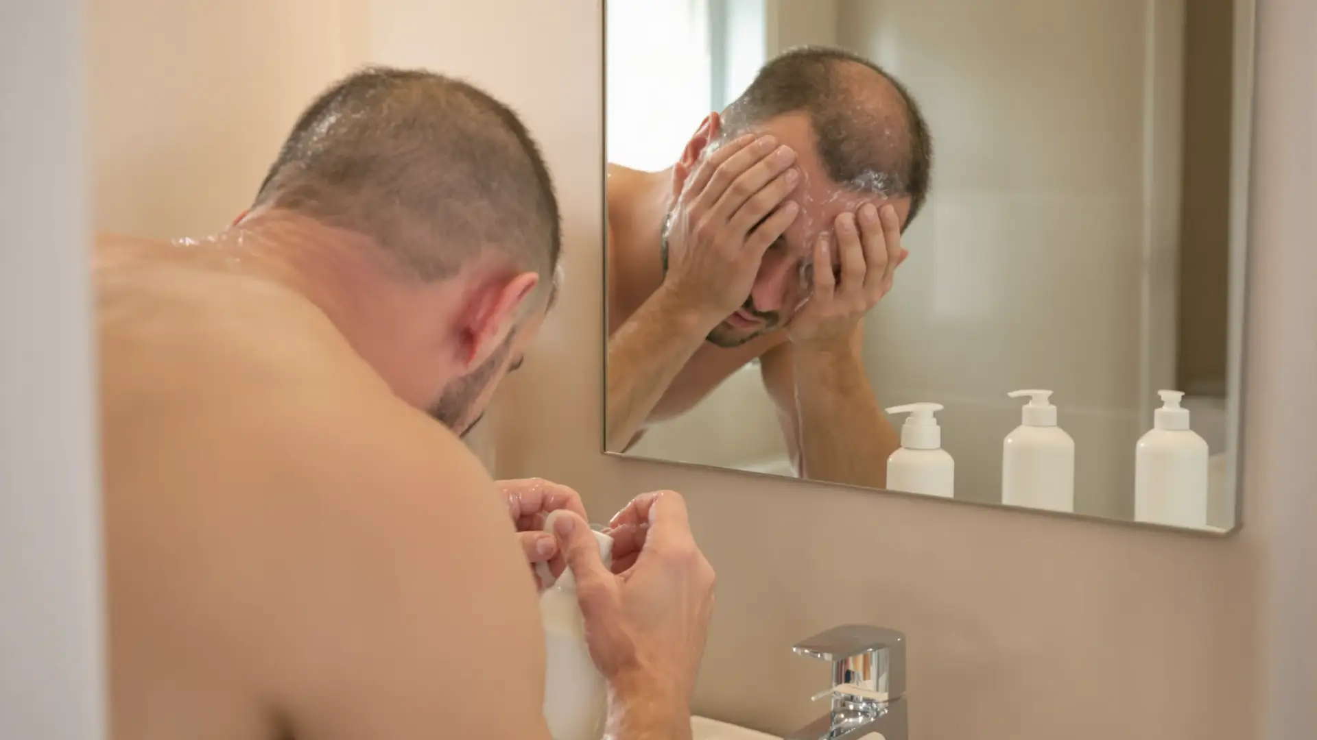 Man rinsing recently transplanted hair over bathroom sink.