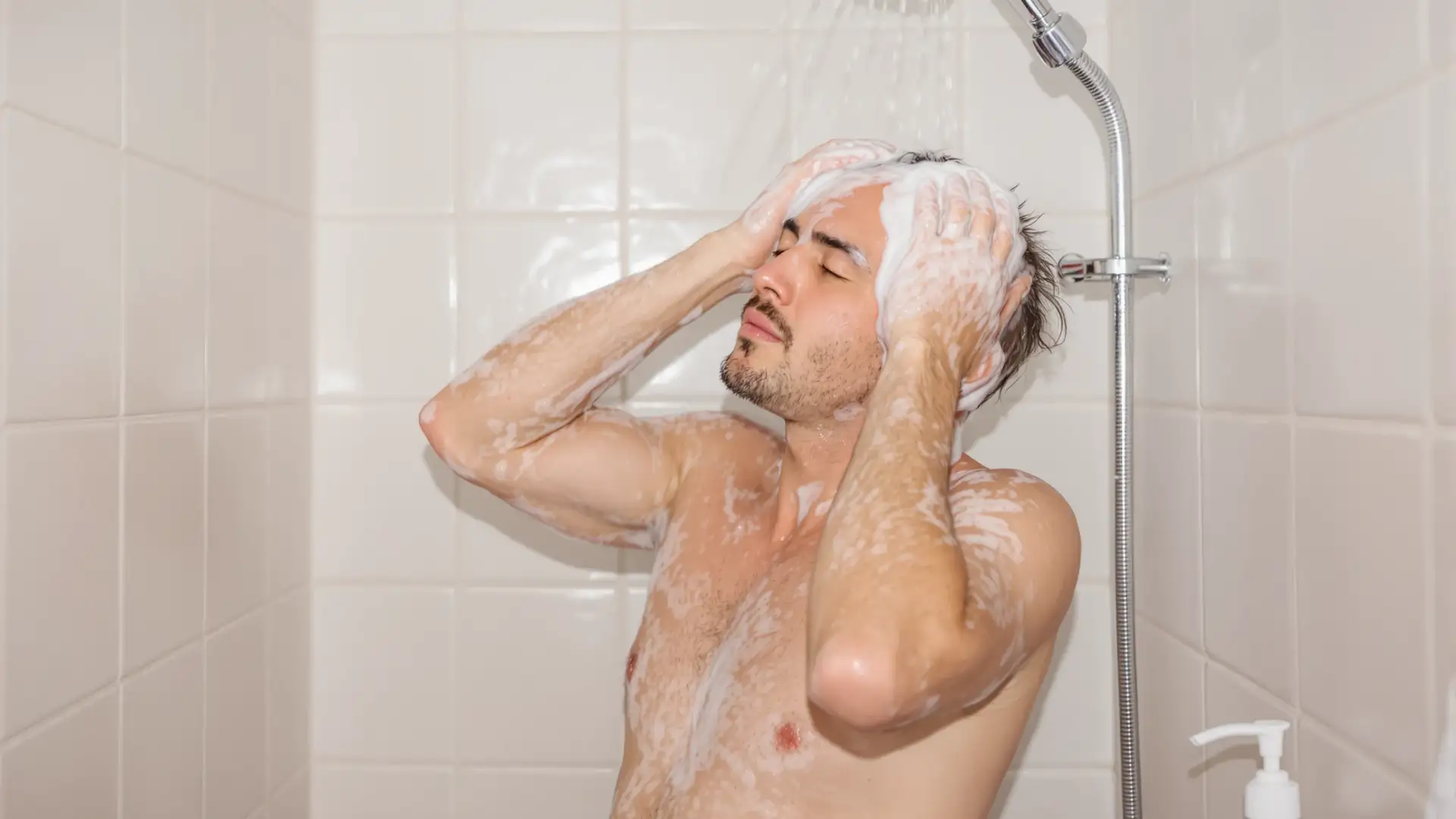 Man washing thinning hair with shampoo in the shower.