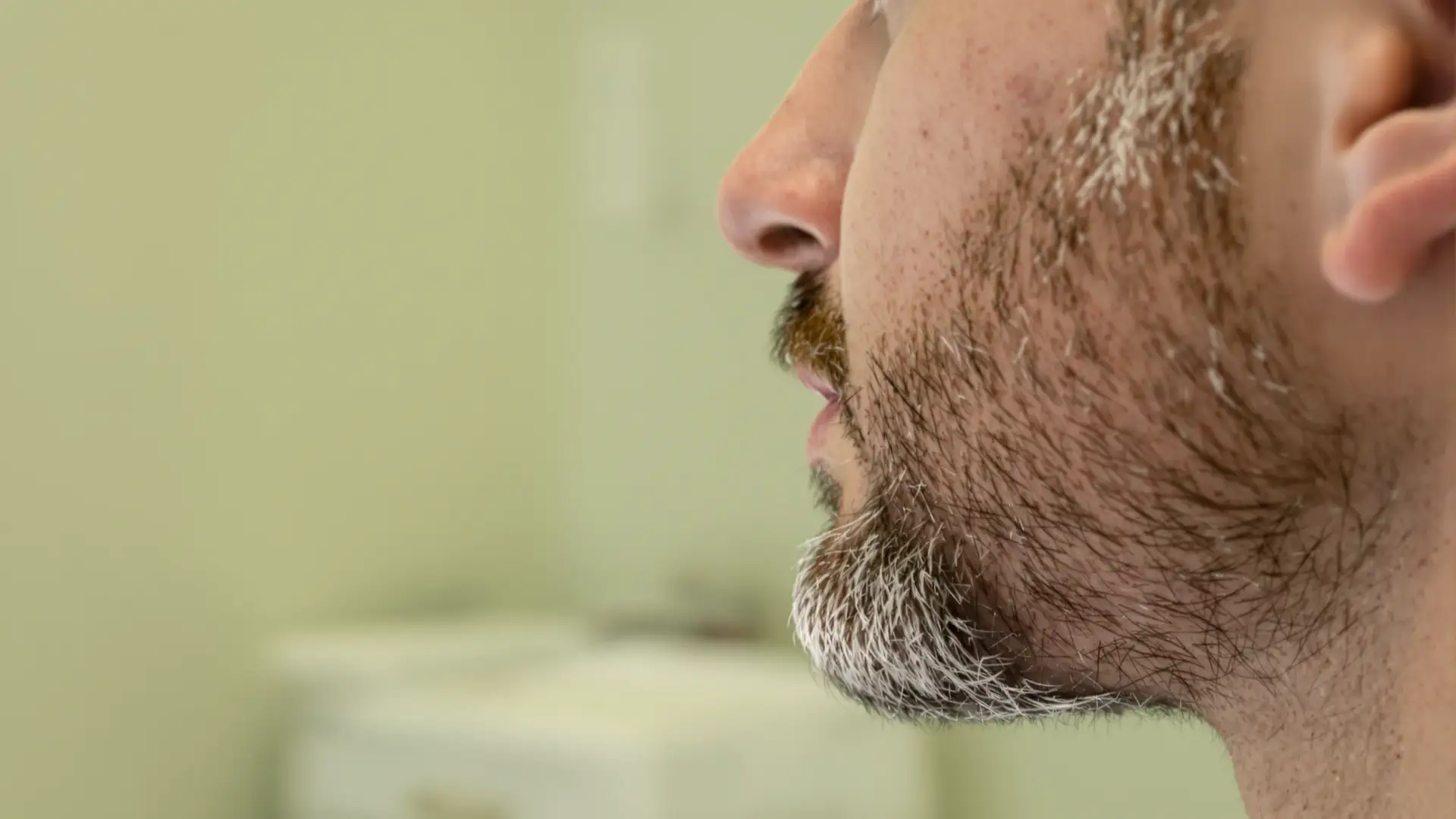 Primo piano del profilo di un uomo con barba folta e pelle del mento in evidenza.