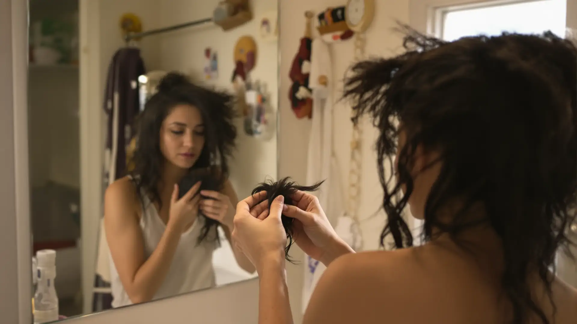 Woman in bathroom looking at loose hair in a brush, worried about shedding.