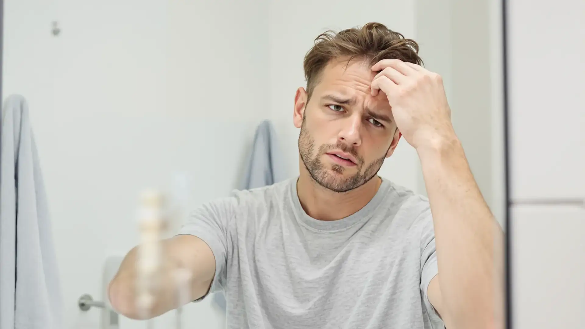 Man checking thinning hair in bathroom mirror