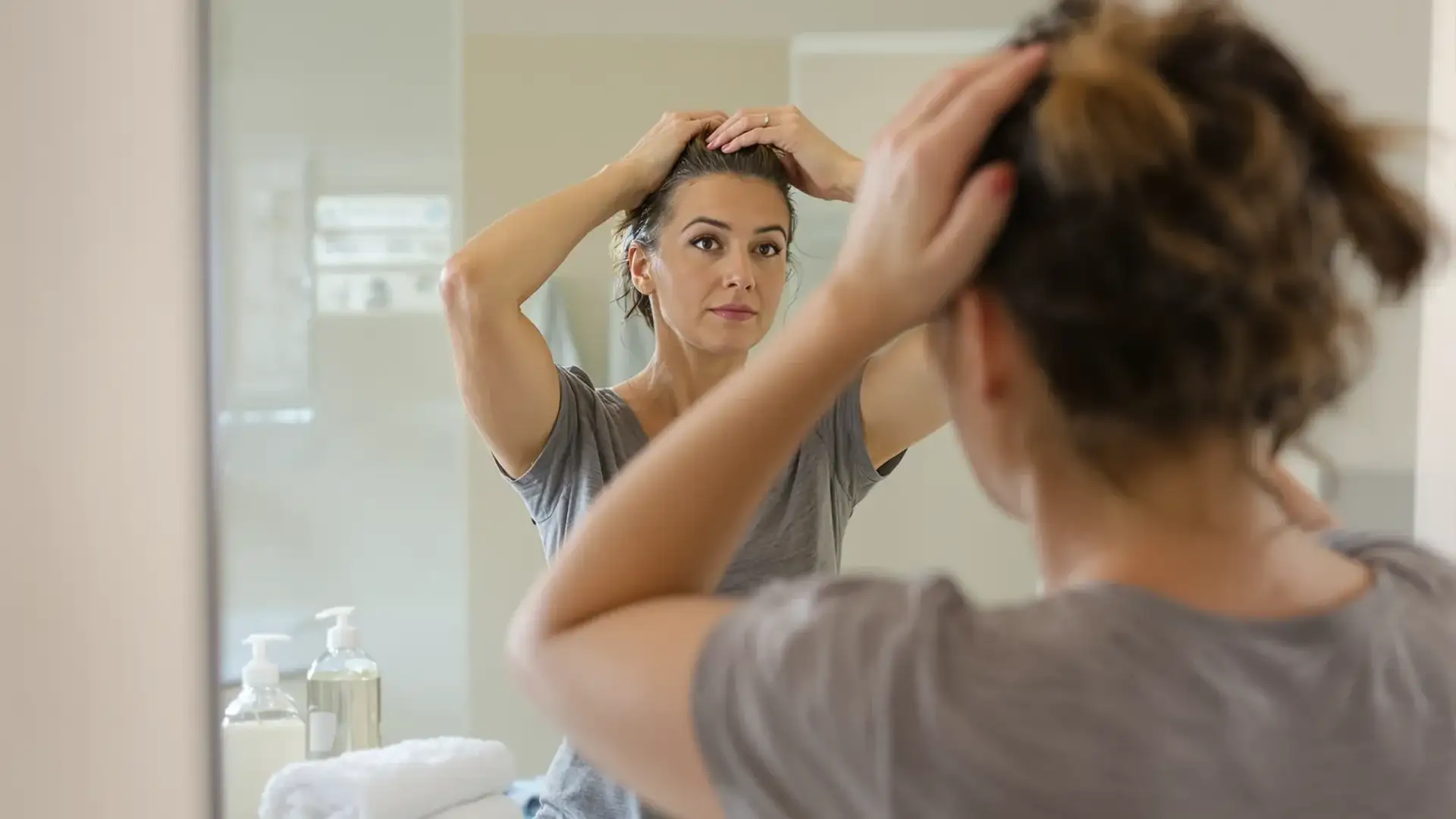 Woman inspecting thinning hair at crown in bathroom mirror