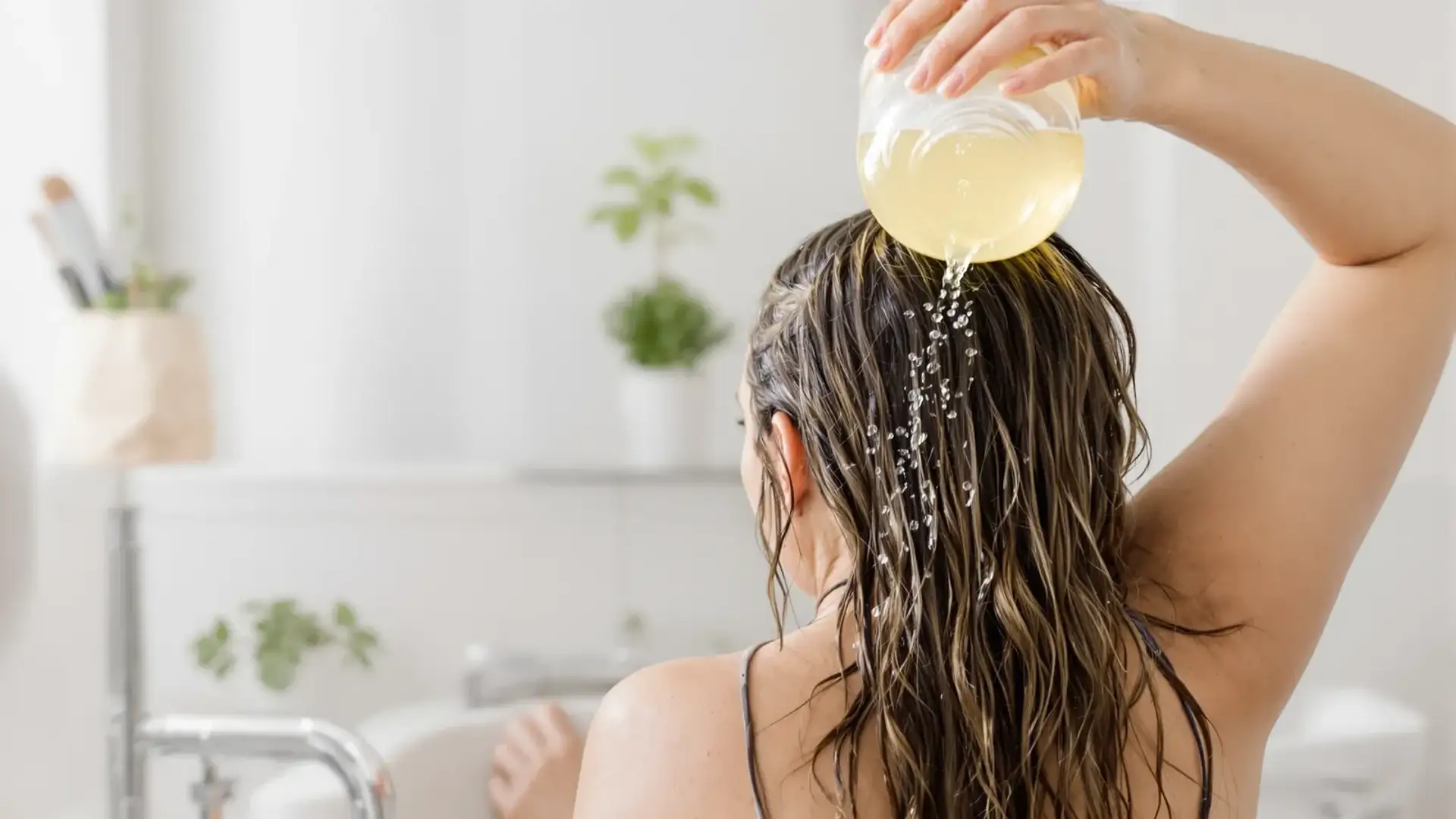 Woman rinsing her wet hair with apple cider vinegar in a bathroom