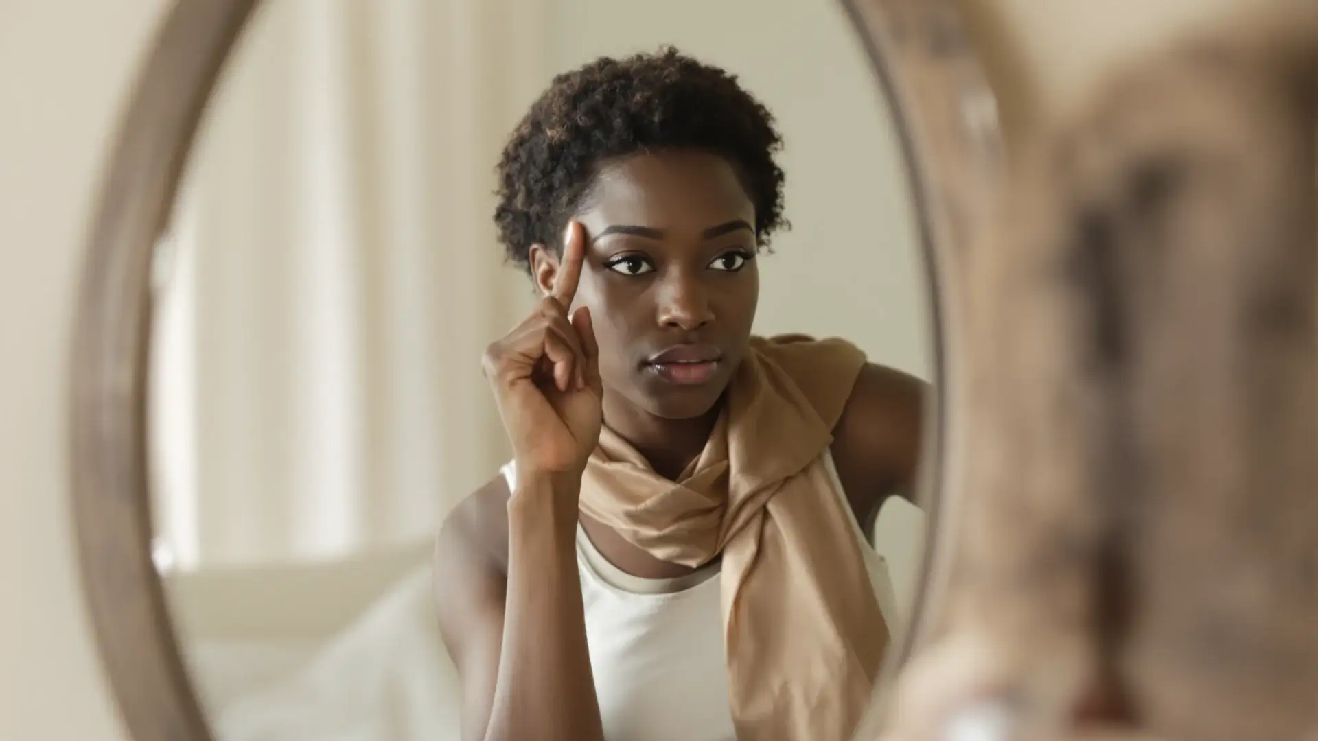 Black woman checking her temple hairline and edges in a bedroom mirror