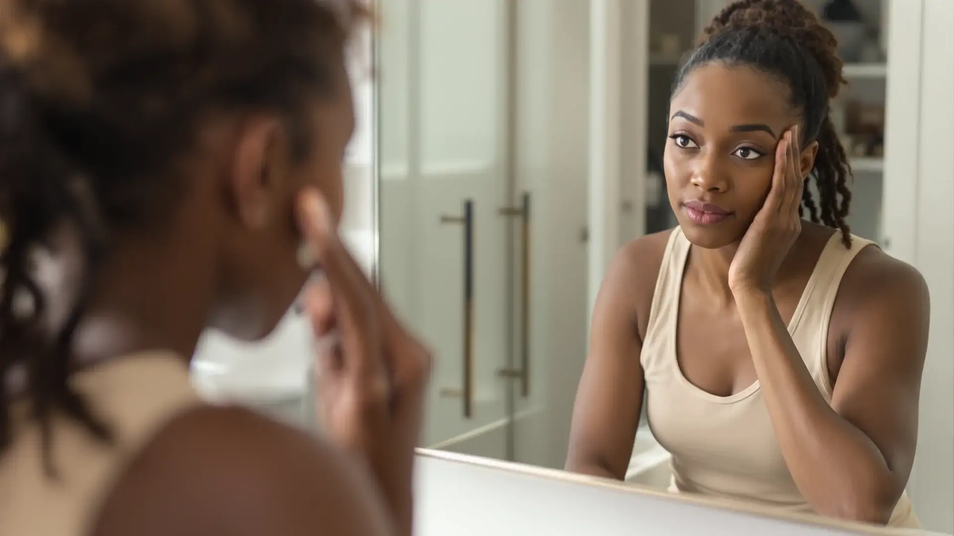 Black woman touching her temple hairline while looking in a mirror