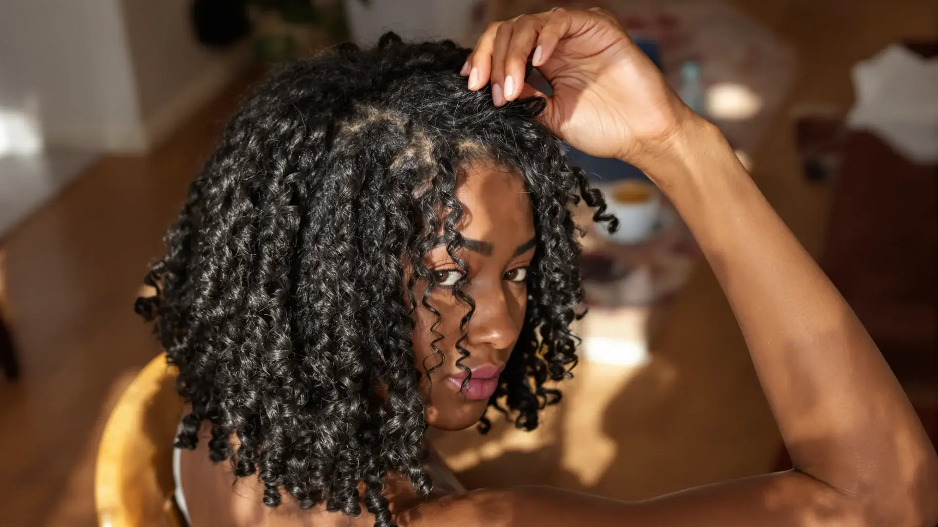 Black woman with 3C corkscrew curls lifting a section to show a wider part