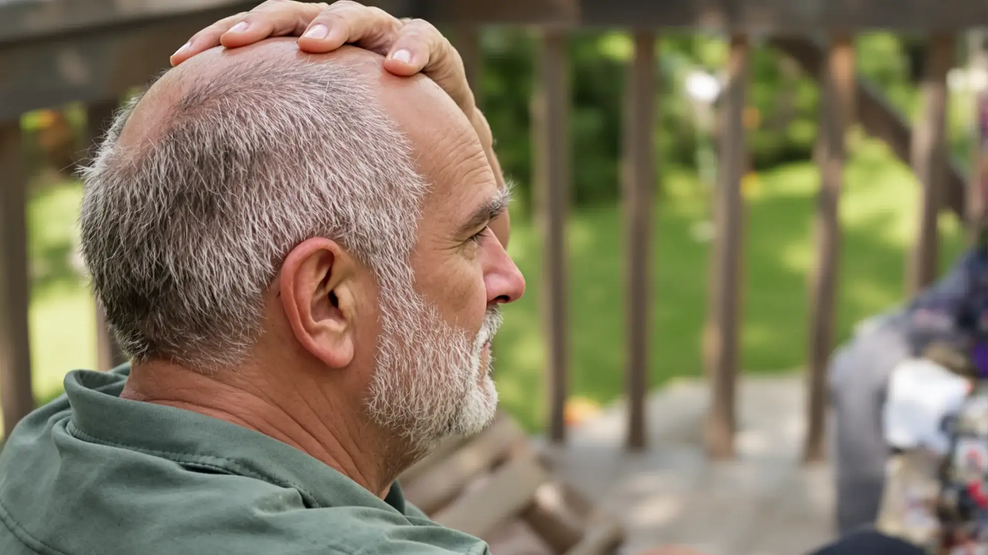 Man in his 50s with a Norwood 7 horseshoe hair pattern sitting on a deck, touching his bald crown