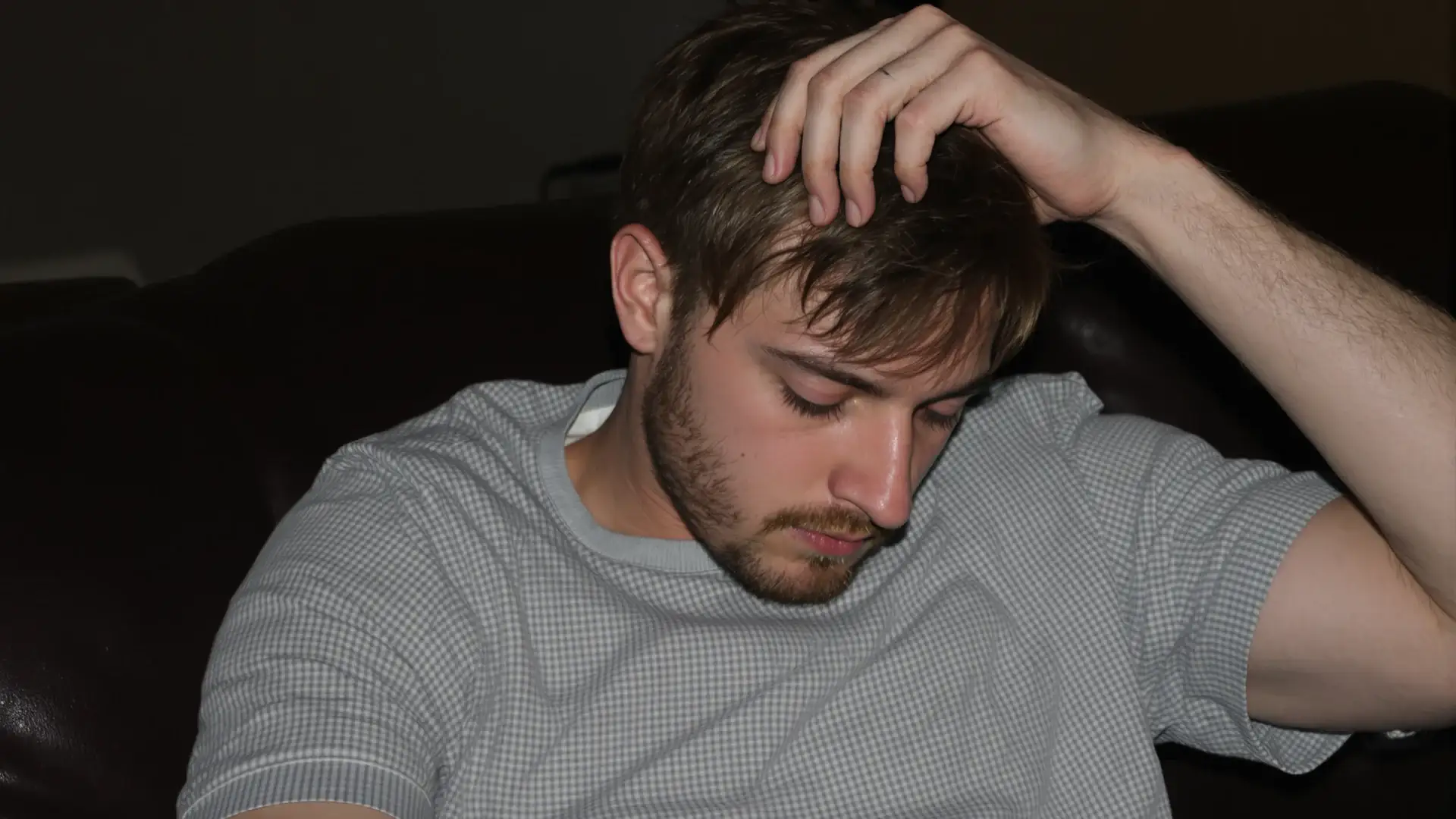 Man with early temple recession touches his hairline on a couch