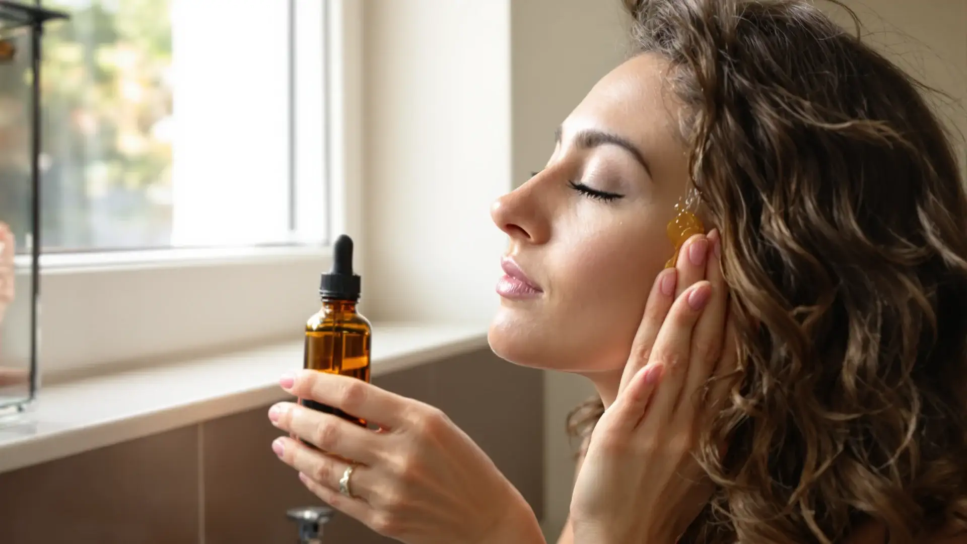 Woman massaging oregano oil blend into her scalp in a sunlit bathroom.