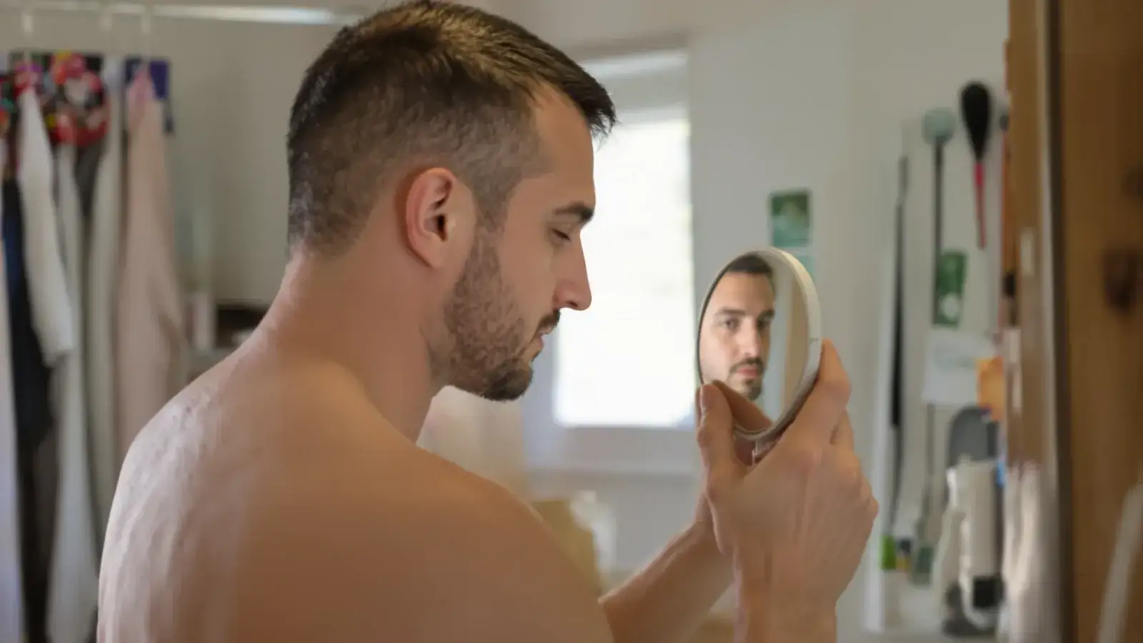 Man inspecting a thinning crown with a hand mirror in a bathroom