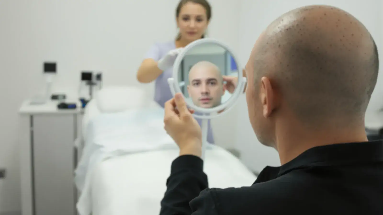 Man with shaved scalp and red grafts in a hair clinic, touching his head.