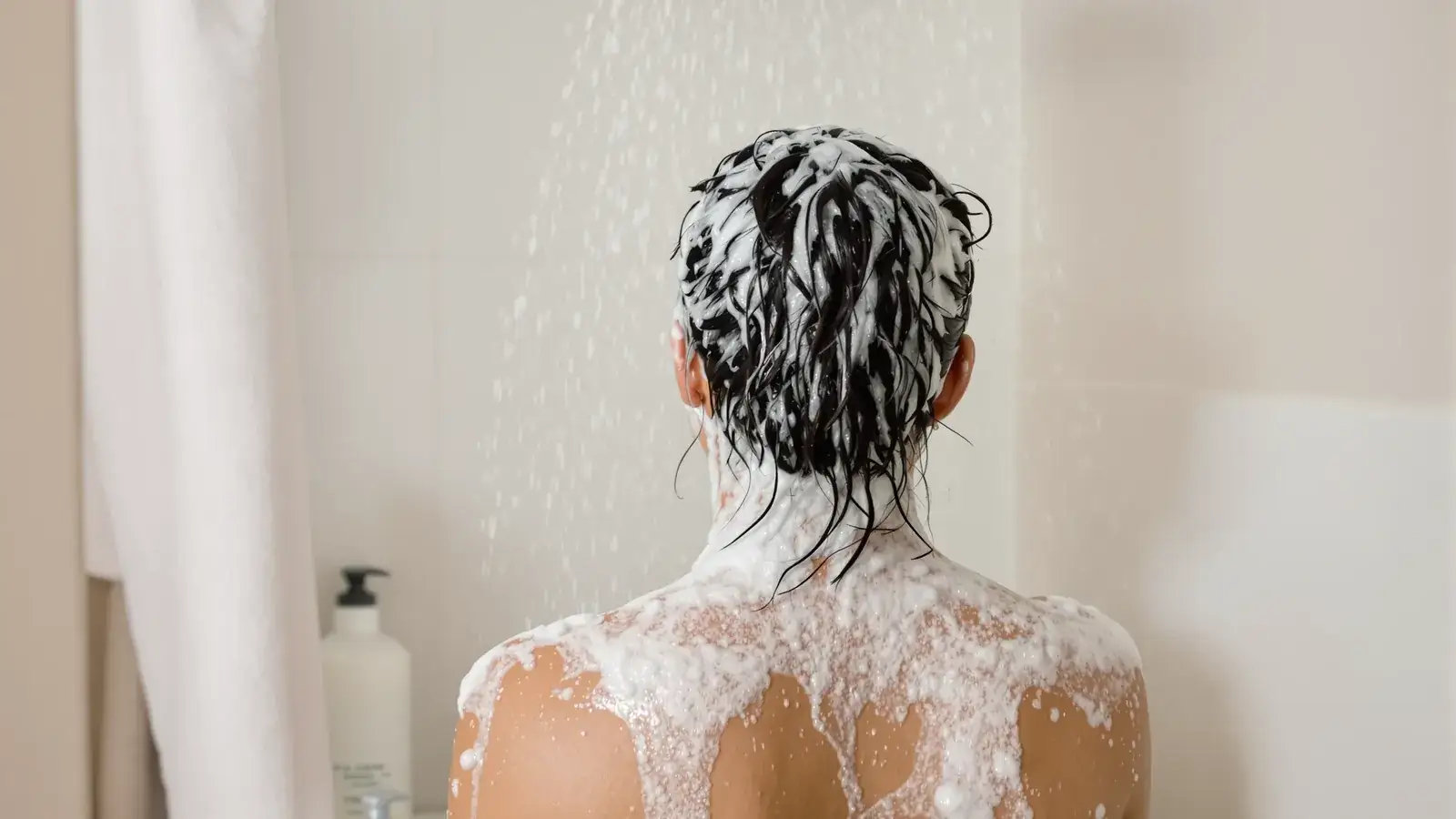 Woman lathering shampoo in the shower with thick suds