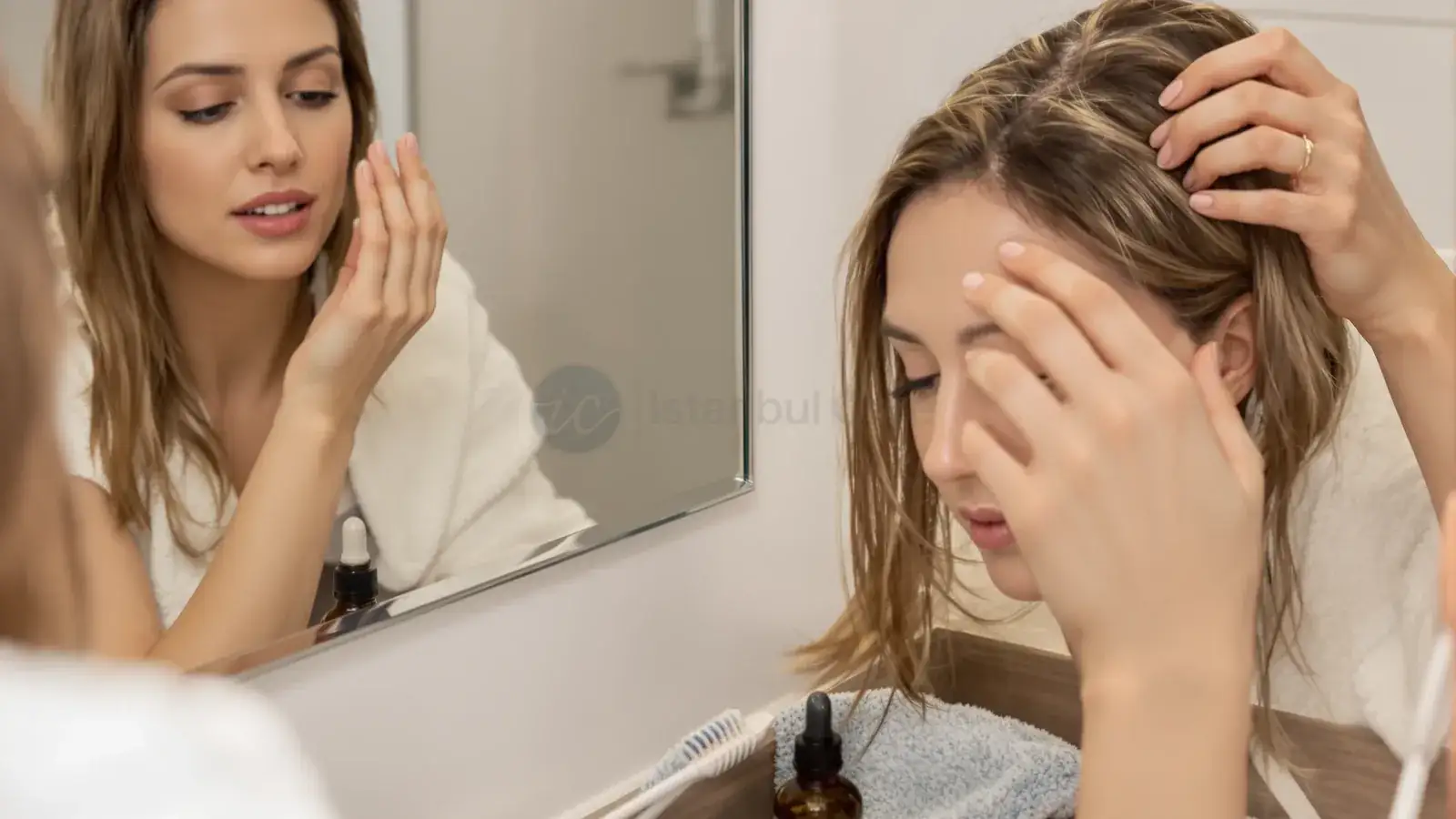 Woman massaging rosemary oil into her scalp in a bathroom.