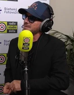 Il cantante Raf fotografato con un cappello mentre parla al microfono in uno studio radiofonico nel 2026. Immagine su licenza: identifica soltanto la persona e non e' prova di alcun trattamento dei capelli.